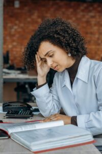 Exhausted woman in office with paperwork, displaying signs of stress.